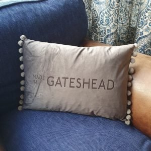A grey velvet cushion engraved with Made in Gateshead with a fun silver pom pom trim.