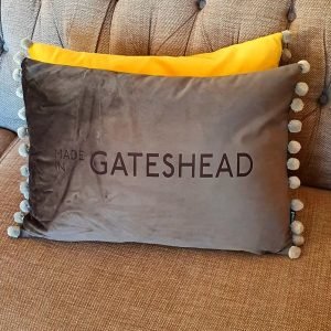 A grey velvet cushion engraved with Made in Gateshead with a fun silver pom pom trim.
