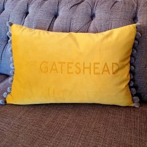 A yellow velvet cushion engraved with Made in Gateshead with a fun silver pom pom trim.