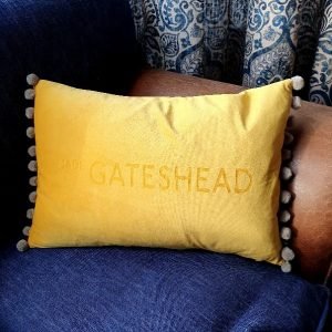 A yellow velvet cushion engraved with Made in Gateshead with a fun silver pom pom trim.