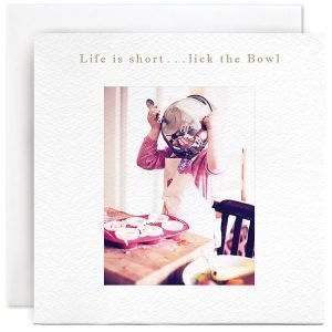Life Is Short, Lick The Bowl Greetings Card. A card with a photograph of a little girls licking a bowl that has been used during baking a cake. The caption reads "Life is short lick the bowl"