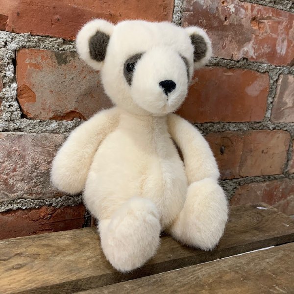 A gorgeous cream wispy teddy bear with grey patches on its small ears and eyes. A black button nose, chunky paws and a tubby belly.