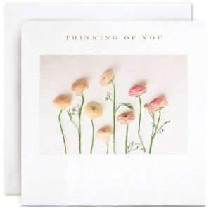 A white square card with a photographic image of some pastel coloured Rannunculus flower and the wording Thinking of you printed above the image