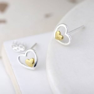 A pair of stud earrings with an open silver hearts with a little gold heart set inside