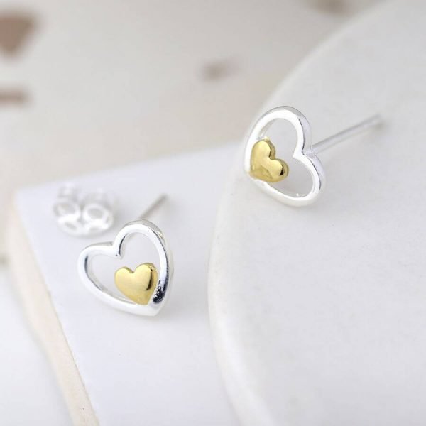 A pair of stud earrings with an open silver hearts with a little gold heart set inside