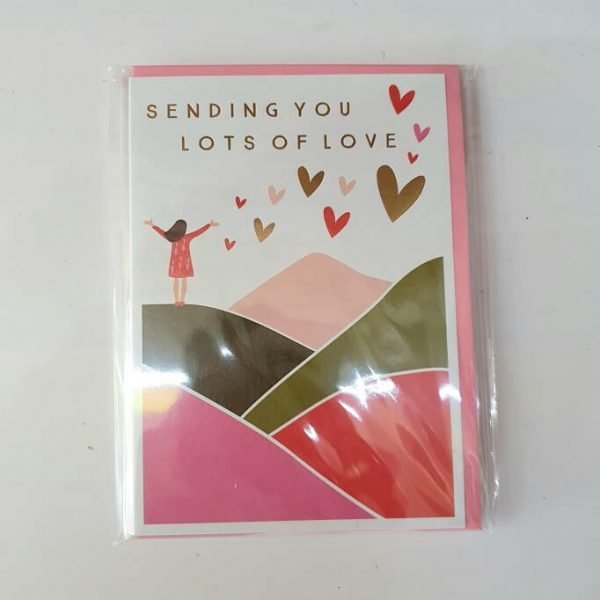 A card for any occasion to raise someones spirit and let them know you care. This greeting card has gold foiling and embossing, it depicts a girl in the hills with lots of hearts and the message sending you lots of love