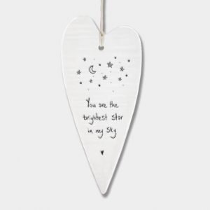 A cream porcelain hanging heart decoration stamped in black with stars and a moon and the words you are the brightest star in my sky