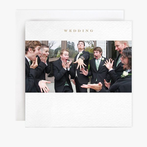 A square card with a photograph of a group of men., One is the groom and he is showing the others his new wedding ring. The others are looking wide mouthed, shocked and excited.