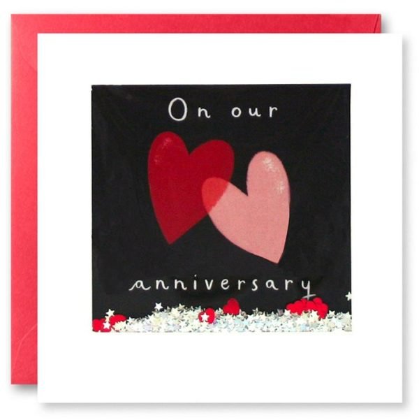 A square card with a white border. The background is black with 2 love hearts printed and the wording On Our Anniversary. This is all behind a clear area of cellophane which has glitter and confetti inside. When you shake the card the confetti moves around.
