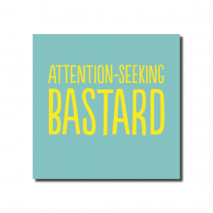 A small square pale blue card with yellow text that says. ATTENTION SEEKING BASTARD