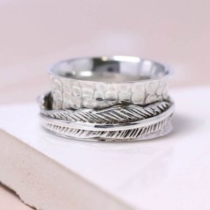 Hand made sterling silver ring with a beaten concave band and two slim connected silver feathers, spinning freely around the band.