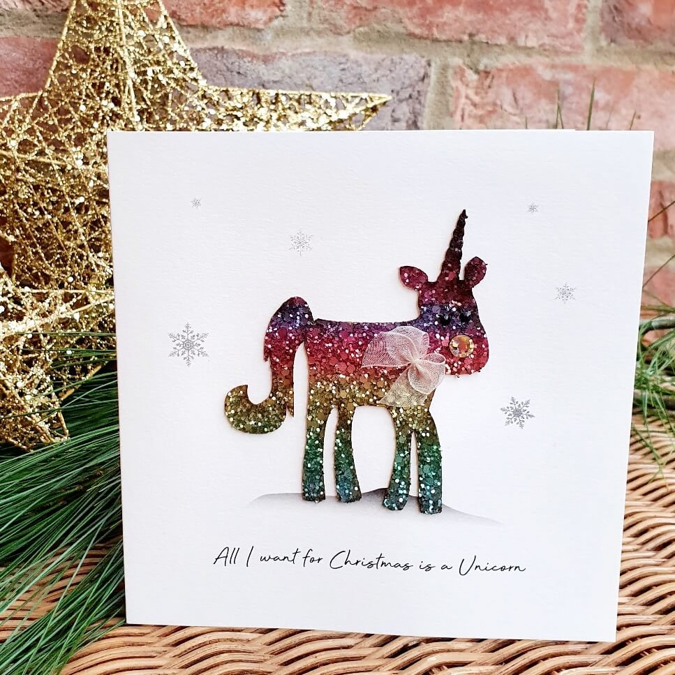 A luxury Christmas card from Five Dollar Shake featuring a Reindeer with a unicorns horn. The reindeer is made of rainbow glitter and has an organza ribbon around his neck. All I want for Christmas is a Unicorn.