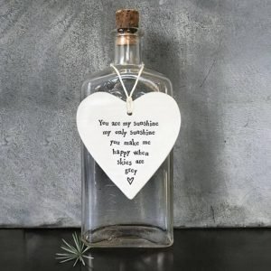 A cream porcelain hanging heart with black stamped writing that reads you are my sunshine my only sunshine you make me happy when skies are grey