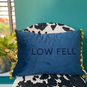 A gorgeous indigo blue cushion with lime green pompoms on each end and the words Made in Low Fell imprinted on it.