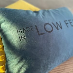 A gorgeous indigo blue cushion with lime green pompoms on each end and the words Made in Low Fell imprinted on it.