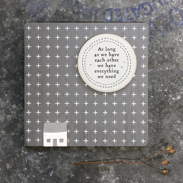 A cute little sign with a dark grey background and a little house on it with a large sun and the words 'As long as we have each other we have everything.'