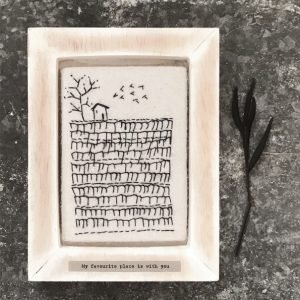 A sweet wooden frame with a square of felt which is embroidered with an image of a field with a tree and a little house. The wording 'My favourite place is with you' printed on it.