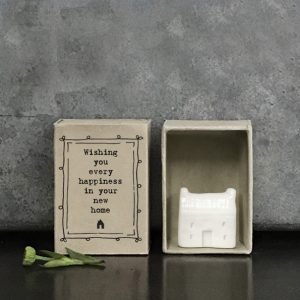 A little porcelain house keepsake which is presented in a cardboard matchbox which has the wording 'Wishing you every happiness in your new home' printed on it.