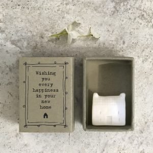 A little porcelain house keepsake which is presented in a cardboard matchbox which has the wording 'Wishing you every happiness in your new home' printed on it.