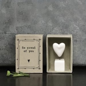 A sweet little white ceramic heart in a pot which is kept in a cardboard matchbox with the wording 'So proud of You' printed on it.