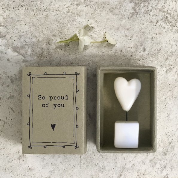 A sweet little white ceramic heart in a pot which is kept in a cardboard matchbox with the wording 'So proud of You' printed on it.