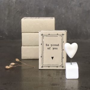 A sweet little white ceramic heart in a pot which is kept in a cardboard matchbox with the wording 'So proud of You' printed on it.