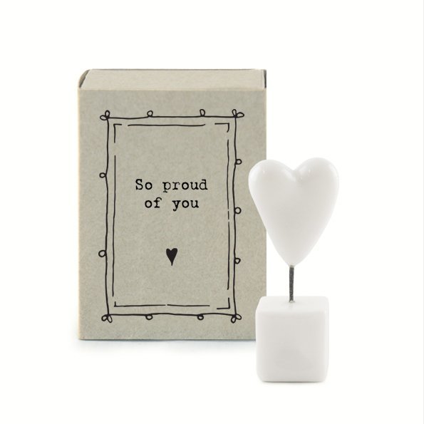 A sweet little white ceramic heart in a pot which is kept in a cardboard matchbox with the wording 'So proud of You' printed on it.
