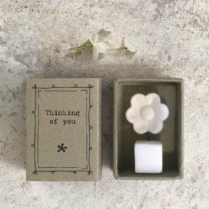 A sweet little white ceramic flower in a pot keepsake in a cardboard matchbox with the words 'Thinking of You' printed on it.