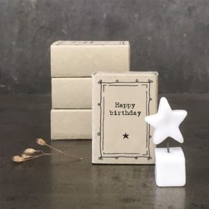A cute little white ceramic star on a little ceramic cube which is presented in a matchbox with the words Happy Birthday printed on it