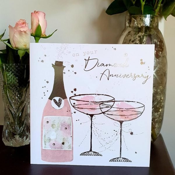 A large square diamond wedding anniversary card with a bottle of champagne and glasses in pinks and silver foil and little crystals