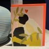 A colourful card with a lovely affectionate couple on it with a love heart printed above them