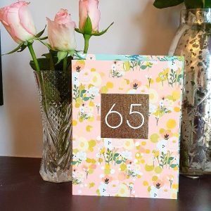 A peach coloured flowery b65th birthday card with a gold panel with a big 65