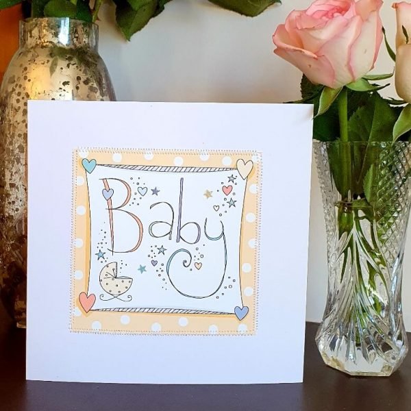 A neutral new baby card with hand drawn illustrations on a peach spotty background and hand stitched edging.