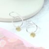 A pair of sterling silver drop earrings which have a hoop design with a scratched gold plated heart on the bottom of it.