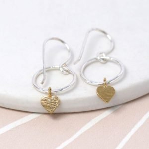 A pair of sterling silver drop earrings which have a hoop design with a scratched gold plated heart on the bottom of it.