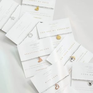 A silver plated bead stretch bracelet with a gold heart charm from Joma Jewellery. The bracelet is presented on a square card with the wording 'A Little Beautiful Friend' printed on it.