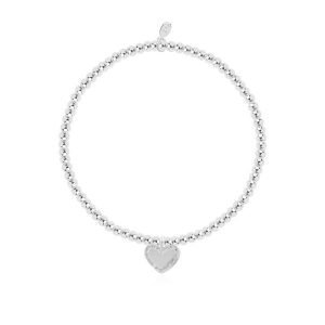 A silver plated bead stretch bracelet with an embellished heart charm from Joma Jewellery. The bracelet is presented on a pink coloured card with the wording A Little Happy Mother's Day printed on it.