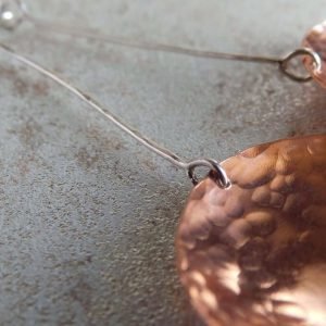 A pair of long drop earrings hand crafted from copper and sterling silver. A long silver wire with a hammered textured copper disc suspended from the end. Presented in a gift box