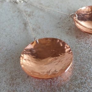 A pair of long drop earrings hand crafted from copper and sterling silver. A long silver wire with a hammered textured copper disc suspended from the end. Presented in a gift box