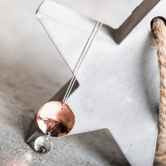 A handcrafted necklace with two hammered discs pendant. A larger copper hammered disc and a smaller sterling silver hammered disc suspended from it. The pendant is on a silver chain.