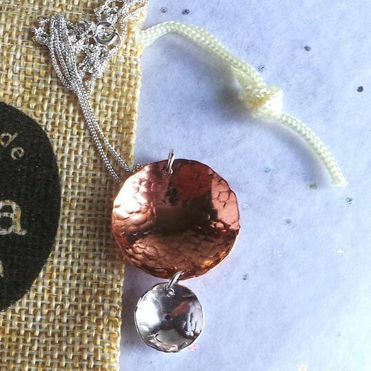 A handcrafted necklace with two hammered discs pendant. A larger copper hammered disc and a smaller sterling silver hammered disc suspended from it. The pendant is on a silver chain.
