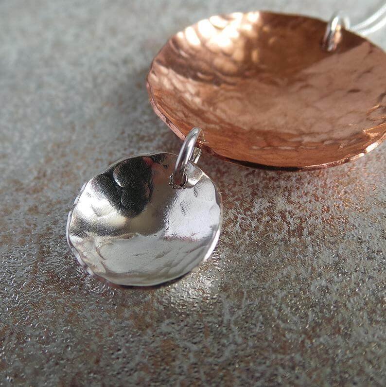 A handcrafted necklace with two hammered discs pendant. A larger copper hammered disc and a smaller sterling silver hammered disc suspended from it. The pendant is on a silver chain.