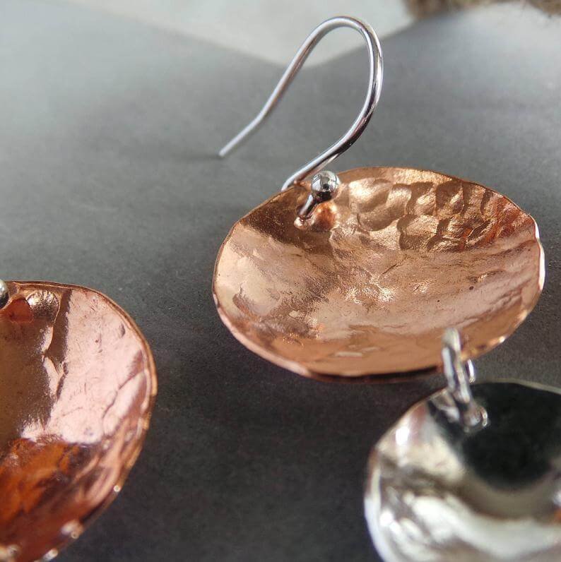 A pair of hand crafted earrings made from copper and sterling silver. Two hammered texture discs suspended from a silver ear wire. The top disc is larger (2cm) and is made of copper, the bottom disc is smaller (1.2cm) and made of silver.