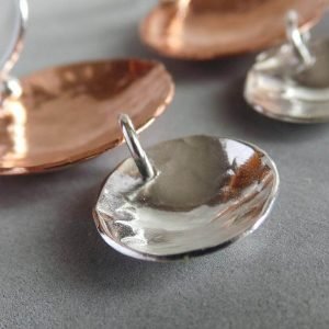 A pair of hand crafted earrings made from copper and sterling silver. Two hammered texture discs suspended from a silver ear wire. The top disc is larger (2cm) and is made of copper, the bottom disc is smaller (1.2cm) and made of silver.