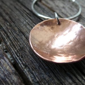 A hand crafted silver and copper mixed metal necklace. A silver hammered circle of silver with a hammered textured copper disc suspended from it. Comes in a gift box