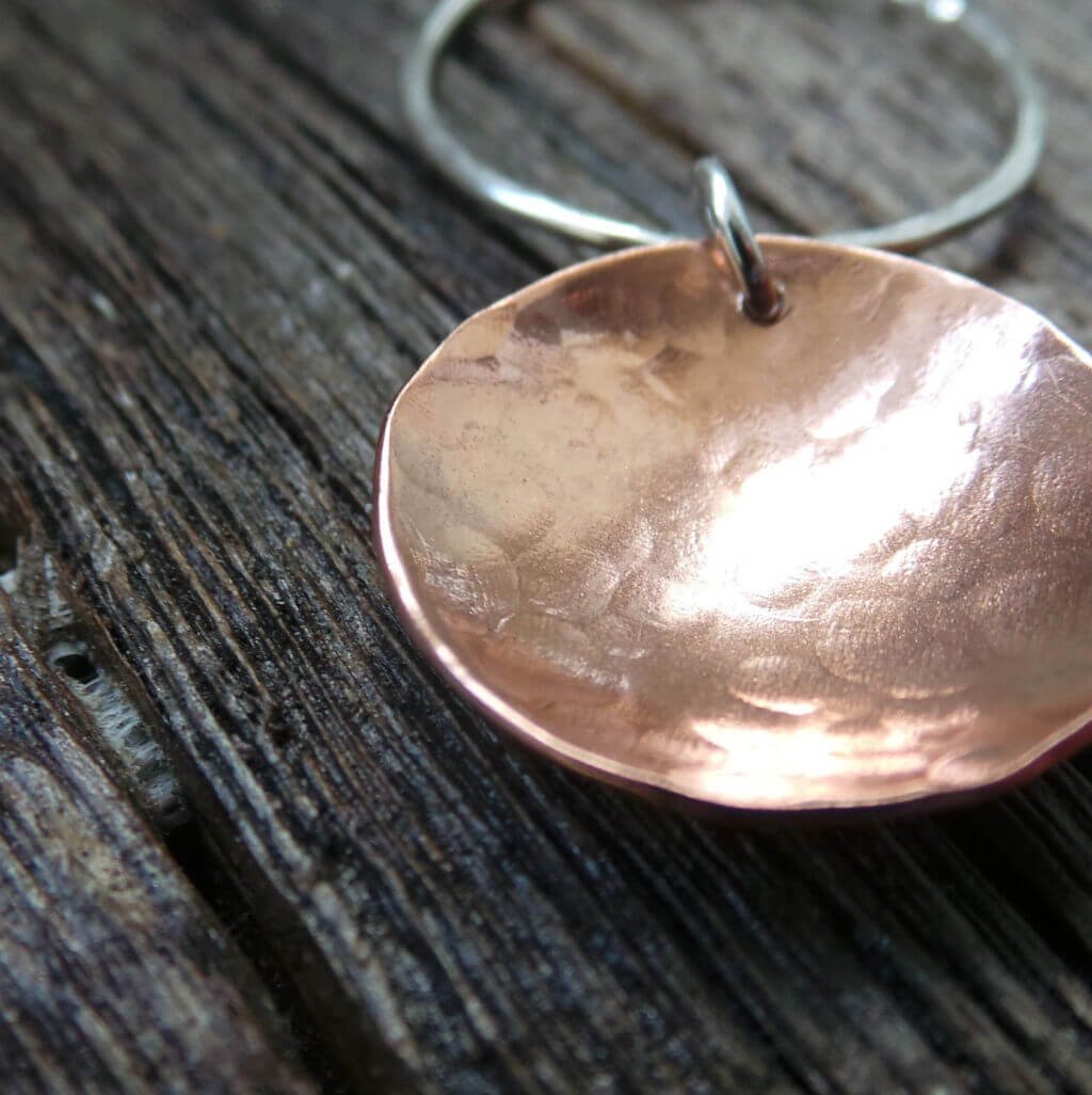 A hand crafted silver and copper mixed metal necklace. A silver hammered circle of silver with a hammered textured copper disc suspended from it. Comes in a gift box