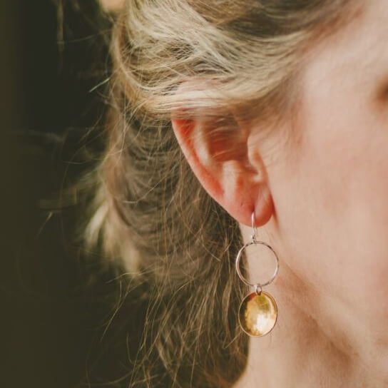 A pair of hand crafted silver and copper mixed metal earrings. A silver ear wire holds a hammered circle of silver with a hammered textured copper disc suspended from it. The earrings have approximately 5cm drop and come in a gift box