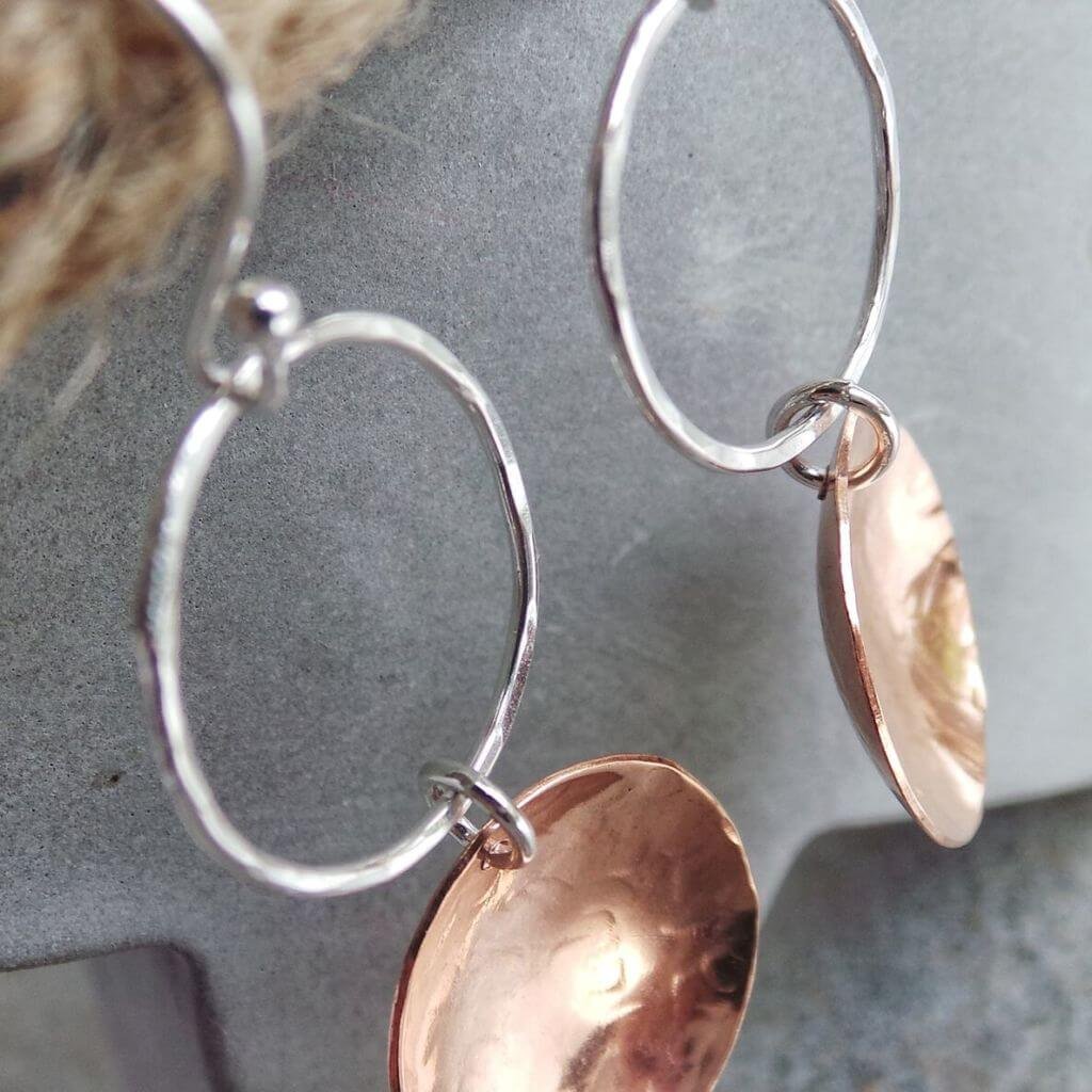 A pair of hand crafted silver and copper mixed metal earrings. A silver ear wire holds a hammered circle of silver with a hammered textured copper disc suspended from it. The earrings have approximately 5cm drop and come in a gift box