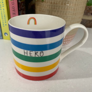 A multi coloured striped bone china mug with the word Hero printed on it. On the inside of the mug a little rainbow is printed.