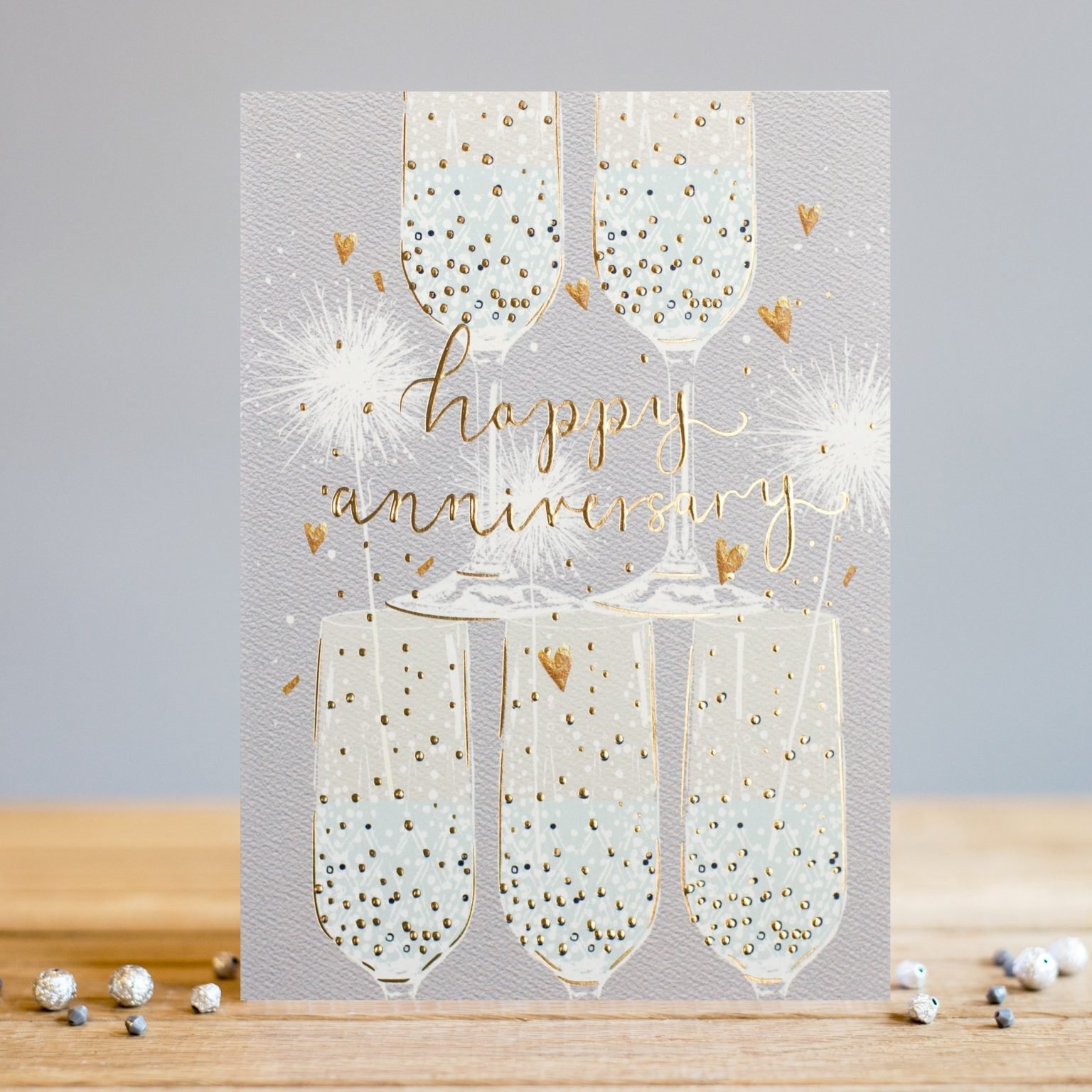 A beautiful card with a stack of champagne glasses with sparkles and hearts all around them. The words Happy Anniversary are embossed, foiled and printed in the centre of the card.